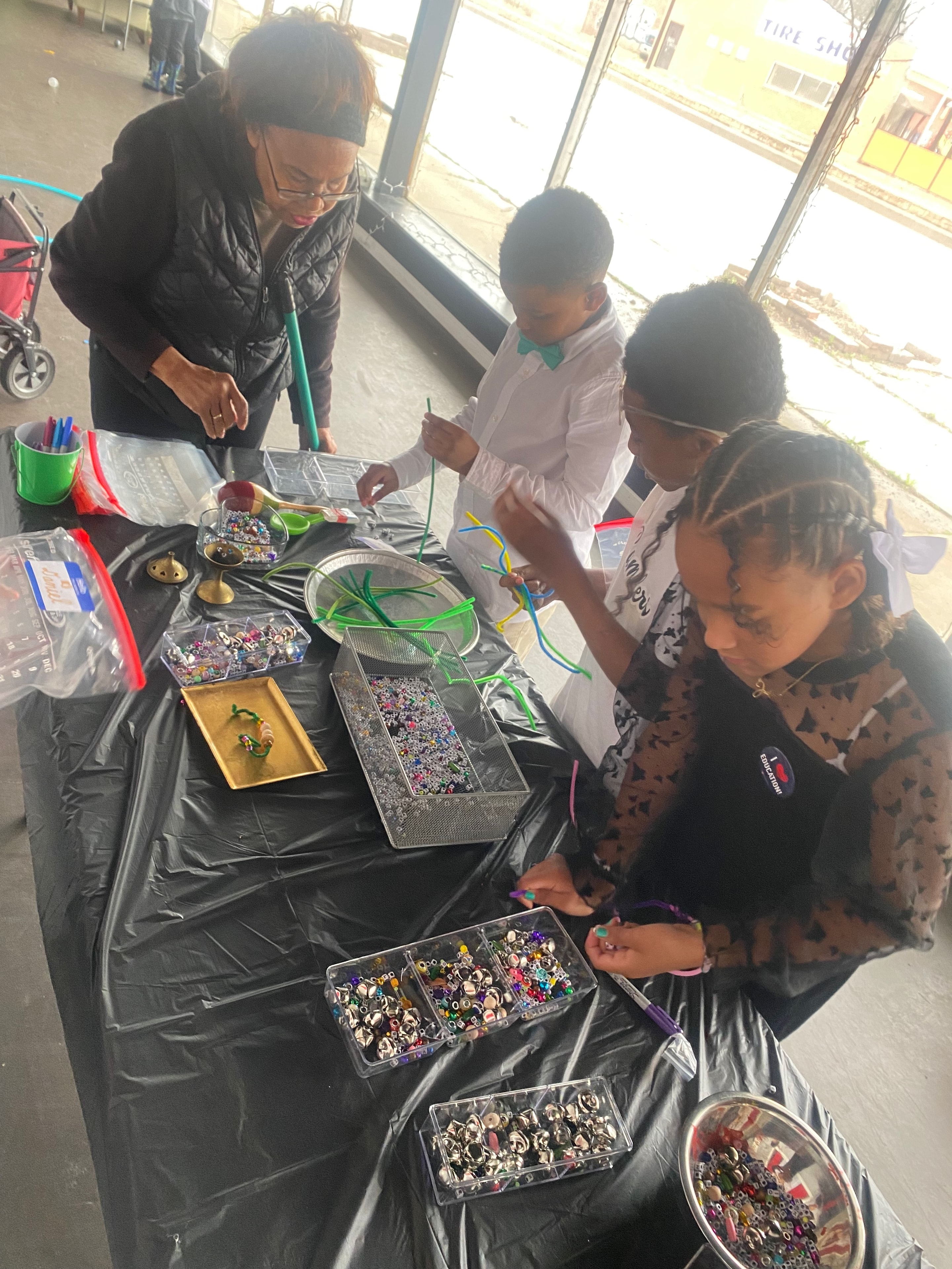 An adult and children creating together at a table with beads and craft materials.
